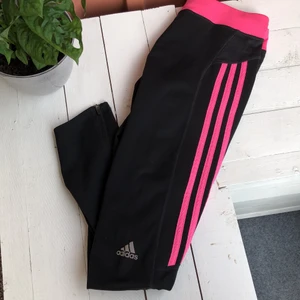 Adidas träningstights strl M - Träningstights från Adidas med rosa revärer. Dragkedja nertill. Finns snörning invändig så de kan dras åt och knytas vid behov. Ej helt långa - se bild 