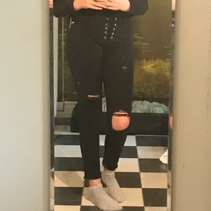 Svart jeans - Svarta jeans med hål på knäna, snörning fram och dragkedja på sidan