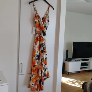 Blommig klänning Nelly stl S - En vit klänning med stora orangea blommor från Nelly i storlek S. Oanvänd så alla lappar finns kvar. Fraktkostnaden tillkommer.