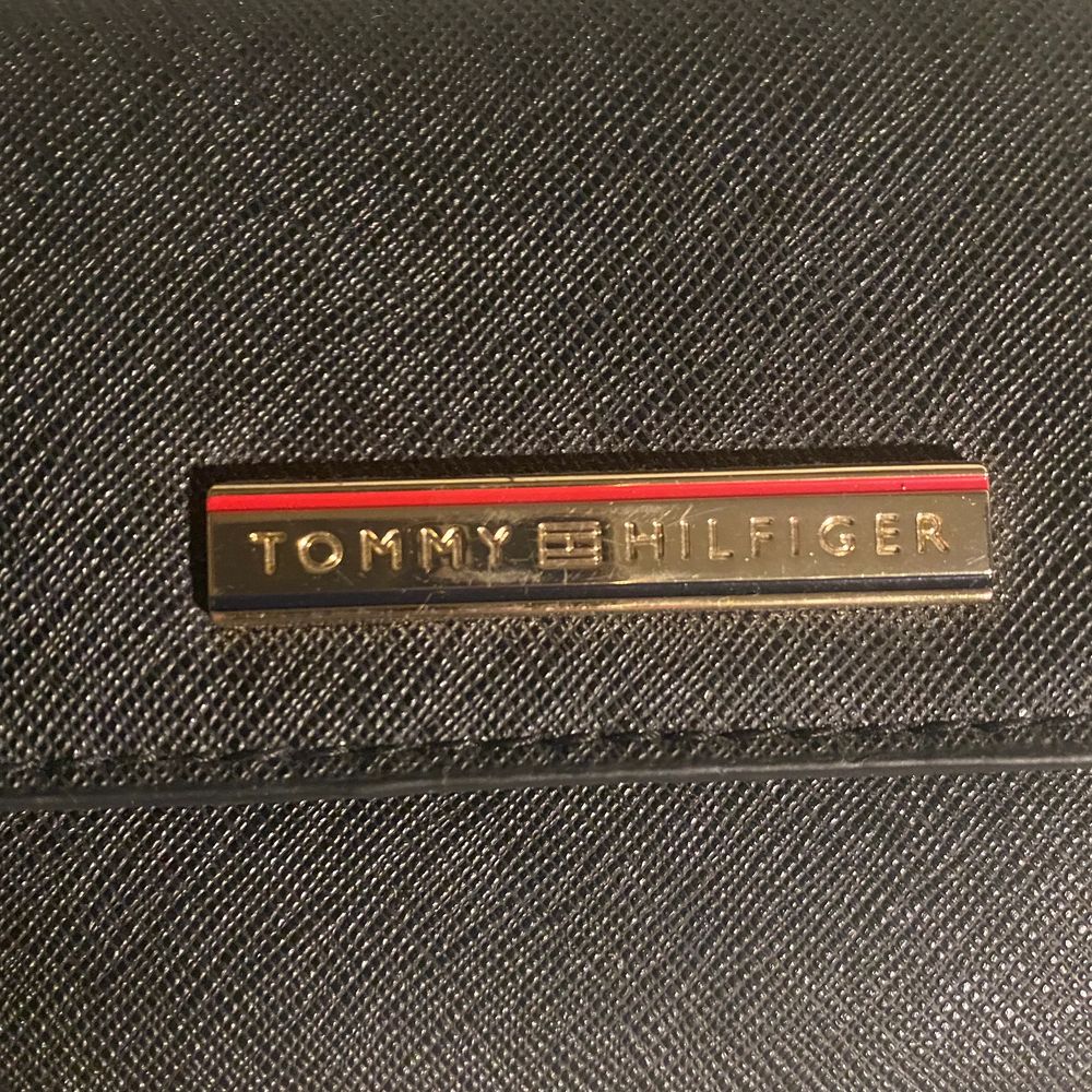 Liten väska från Tommy Hilfiger med långt axelband. Har en ficka med dragkedja och en som öppnas och stängs med knapp. Sparsamt använd och i jättefint skick. Äkta såklart!. Väskor.