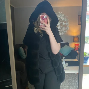 Svart fake päls väst - En fin fake pälsväst, fint skick. Storlek M/L. Med luva och 2 fickor. Jag köpte den på miinto för länge sen, hittade den inte på sidan.