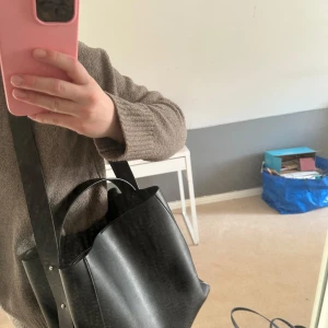 Svart axelväska i skinn - Säljer en stilren svart axelväska i skinn med bred axelrem och praktiskt innerfack med dragkedja. Väskan har en enkel och modern design som passar till många olika outfits. Perfekt storlek för att få plats med allt du behöver till vardags☺️