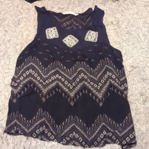 Topp från ONLY - Säljer en snygg ärmlös topp med ett unikt mönster i mörkblått och vitt. Toppen har en lös passform och är perfekt för varma dagar. Den har ett geometriskt mönster som ger en bohemisk känsla.