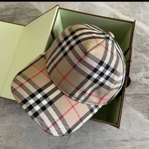 Rutig keps från Burberry - Snygg rutig keps från Burberry i klassiskt beige, svart och rött mönster. Kepsen har justerbar rem baktill för perfekt passform och en broderad logotyp på baksidan. Perfekt för en stilren look.