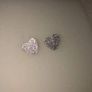 Glittriga hjärtformade örhängen - Säljer ett par glittriga hjärtformade örhängen i silver. Perfekta för att ge en extra touch av glamour till din outfit. De är små och eleganta, vilket gör dem lätta att bära hela dagen.