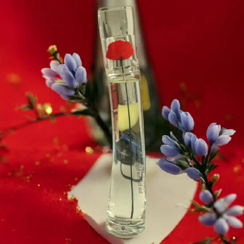Elegant parfym i en smal, genomskinlig glasflaska med en röd blomma på toppen. Flaskan har en modern och stilren design som passar perfekt på sminkbordet.. Perfume.