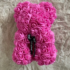 Rosa nallebjörn med rosor - Charmig nallebjörn täckt av rosa rosor, perfekt som en romantisk present eller dekoration. Nallen saknar två rosor på sidorna.