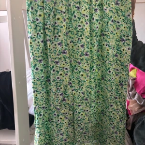 Grön blommig kjol - Säljer en härlig grön kjol med blommigt mönster. Perfekt för sommarens varma dagar. Kjolen har en luftig passform och är gjord i ett lätt material. Köpt från Lindex och använd en gång