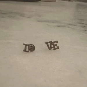 Silvriga örhängen LOVE - Snygga silvriga örhängen med texten 'LOVE'. Perfekta för att ge en subtil men stilfull touch till din outfit. Passar bra till både vardag och speciella tillfällen.