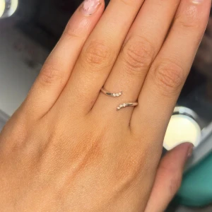 Elegant guld ring med stenar - Säljer en elegant guld ring med en öppen design och små gnistrande stenar på ändarna. Perfekt för att ge en subtil men lyxig touch till din stil. Passar bra till både vardag och speciella tillfällen.