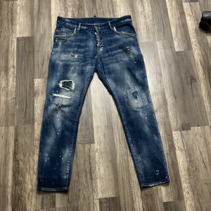 Blå jeans från Dsquared2 - Säljer ett par coola blå jeans från Dsquared2 med slitna detaljer och färgstänk. De sitter perfekt på mig och jag är 176 cm lång . Pris kan förhandlas vid intresse 