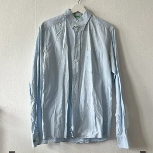 Ljusblå ETON skjorta med knappar - Säljer en stilren ljusblå ETON skjorta med klassisk krage och knappar framtill. Skjortan har en bröstficka och långa ärmar med knappstängning vid ärmsluten. Perfekt för en snygg och uppklädd look. 39/M Slim
