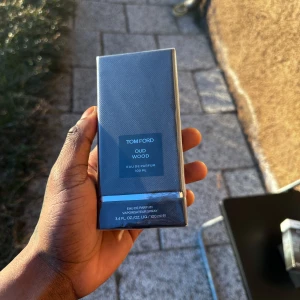 Tom Ford Oud Wood Eau de Parfum 100 ml - Säljer en elegant och lyxig parfym från Tom Ford, Oud Wood, i en 100 ml flaska. Förpackningen är stilren och mörk, vilket speglar doftens exklusiva och mystiska karaktär. Perfekt för den som vill ha en sofistikerad och unik doftupplevelse.