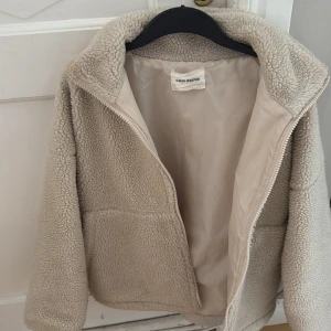 Beige teddyjacka från Carin Wester - Mysig beige teddyjacka från Carin Wester. Jackan har en dragkedja framtill och två stora fickor. Perfekt för kyliga dagar när du vill hålla dig varm och stilren.