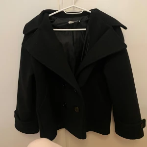 Svart kappa med knappar - Snygg svart kappa med fyra svarta knappar. Från designbysi i storlek XS/S. Sitter superfint på och är perfekt för utgång/sen sommarkväll/middagar!