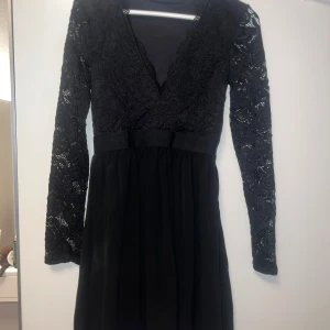 Svart spetsklänning från Nelly - Elegant svart klänning från Nelly med v-ringning och spetsdetaljer. Klänningen har långa ärmar och en smickrande passform.  Säljes pga att den är för liten. Endast använd någon enstaka gång och köpt för några år sedan på Nelly.com. Inga defekter. Perfekt till fester men även andra tillfällen 💕