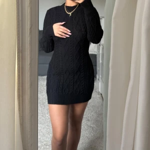 Svart stickad klänning med öppen rygg - Snygg svart stickad klänning med ett stilrent flätmönster. Klänningen har en öppen rygg och långa ärmar, vilket ger en elegant touch. Perfekt för kyligare dagar när du vill vara både varm och chic.