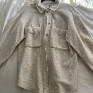 Beige overshirt från & Other Stories - Säljer en stilren beige overshirt från & Other Stories. Jackan har en klassisk krage, knappar framtill och två stora fickor på bröstet. Perfekt för lager-på-lager-stil