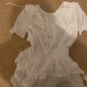 Vit klänning från Gina Tricot - Säljer en söt vit klänning från Gina Tricot med volanger och korta ärmar. Klänningen har en luftig design och är perfekt för varma dagar. Den är gjord i ett lätt material som ger en skön känsla. Perfekt för sommarens alla tillfällen!