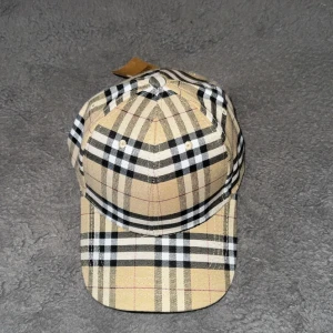 Rutig keps från Burberry - Snygg rutig keps från Burberry i beige, svart och vit. Perfekt för att ge din outfit en klassisk touch. Kepsen har en justerbar rem för bästa passform.