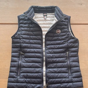 Mörkblå Colmar väst - Snygg mörkblå colmar väst med dragkedja och två praktiska fickor framtill. Skick 8/10 använd i en sommar. Perfekt nu till våren och sommaren. Säljer pga för liten, självklart äkta. Skriv vid intresse eller om frågor.