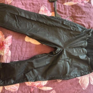 Svarta byxor från H&M - Snygga svarta byxor från H&M i syntetmaterial. De har en strech passform och resår i midjan för extra komfort. Perfekta för en stilren look.