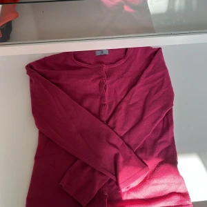 Röd kofta med knappar - Säljer en stilren röd kofta med knappar framtill. Perfekt för att hålla sig varm under kyliga dagar. Koftan har långa ärmar och en klassisk design som passar till det mesta.