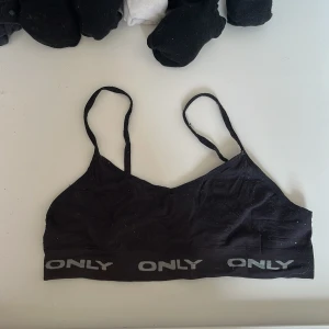 Svart linnetopp från ONLY - Säljer en svart linnetopp från ONLY med smala axelband och elastisk kant med logotyp. Perfekt för en avslappnad stil.