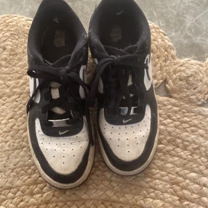 Nike Air Force i svart och vit - Säljer ett par klassiska Nike Air Force sneakers i svart och vit. Skorna har en stilren design med snörning och den ikoniska Nike-loggan på sidan. Perfekta för en casual look.  Finns defekter!
