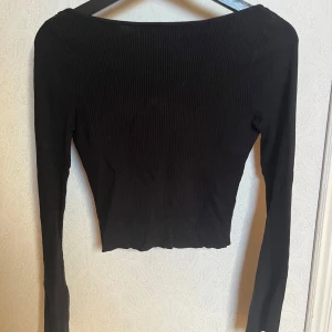 Svart ribbad topp - Snygg svart ribbad topp med lång ärm och djup urringning i ryggen. Perfekt för en stilren look.