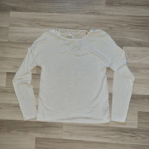 Vit långärmad tröja med knytning bak - Säljer en stilren vit långärmad tröja med knytning bak i nacken. Perfekt för en avslappnad look. Tröjan är i en mjuk och bekväm kvalitet.