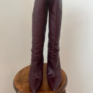 Vinröda/bruna stövlar med spetsig tå storlek 39 - Snygga vinröda/bruna stövlar i skinn med spetsig tå och klack. Perfekta för att ge en elegant touch till din outfit. De har en stilren design som passar till många tillfällen. Sköna att gå i! Storlek 39 från Zara. 