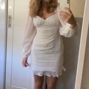 Vit klänning från NLY Trend - Säljer en vit klänning från Nelly med långa ärmar och volangdetaljer. Klänningen har en v-ringad design och dragkedja i ryggen. Perfekt för speciella tillfällen! Endast använd en gång och därav i nyskick 