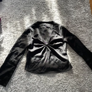 Svart långärmad topp - Snygg svart långärmad topp med en elegant knutdetalj framtill. Perfekt för en stilren look. Silkes liknande material. Storlek s