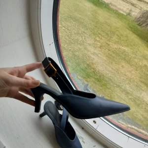 Mörkblå pumps / klackskor  med spetsig tå - Snygga mörkblå klackskor med spetsig tå. Skorna har en elegant rem med spänne runt ankeln för extra stil och komfort. Bara använda en gång. Storlek 38 men fungerar nog bra om för 37. 