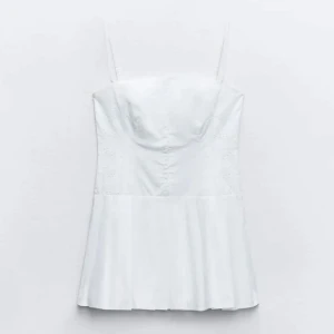 Vit klänning från Zara - Säljer en stilren vit klänning från Zara med smala axelband och en kort design. Klänningen har en enkel och elegant look, perfekt för sommarens varma dagar. Tillverkad i ett lätt och bekvämt material.