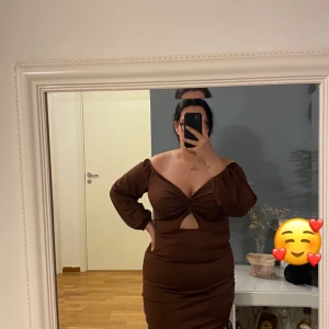 Brun ribbad klänning med knyt - Snygg brun klänning i ribbat material med knytning framtill. Den har trekvartsärmar och en smickrande v-ringad design. Perfekt för en stilren look.