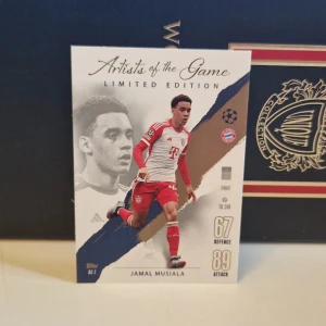 Artists of the Game Limited Edition fotbollskort - Limited Edition fotbollskort från Topps 'Artists of the Game' med motiv av en spelare i FC Bayern München. Kortet har en elegant design med spelaren i aktion och klubbens logotyp. Perfekt för samlare och fotbollsfans.