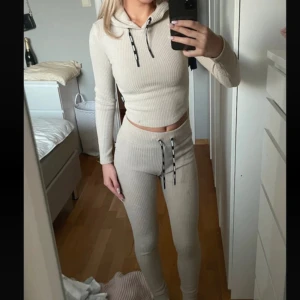 Beige ribbat set - Säljer en beige ribbad set med tights och hoodie med långa ärmar och snörning i huvan. Tröjan är croppad och har en tight passform, perfekt för en stilren look. Passar bra till både vardag och avslappnade tillfällen.