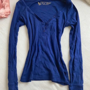 Blå långärmad topp från Victoria’s Secret - Säljer en snygg blå långärmad topp från Victoria’s Secret. Toppen har en v-ringning med knappar och är tillverkad i ett mjukt material. Perfekt för en avslappnad stil. Tillverkad i Sri Lanka.