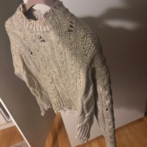Beige stickad tröja från Zara - Säljer en beige stickad tröja från Zara med flätstickat mönster. Tröjan har långa ärmar och en ribbad kant vid halsen och ärmsluten. Perfekt för kyliga dagar!