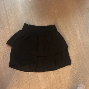 Svart kjol från ONLY - Snygg svart kjol från ONLY med volangdetaljer. Perfekt för en stilren look. Den har en elastisk midja för extra komfort.