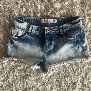 Blå lågmidjade jeansshorts med spetsdetalj - Snygga blå jeansshorts från Hotpant med en cool tvättad look och spetsdetaljer vid bensluten. Perfekta för sommardagar och festivaler. De har en knapp och dragkedja framtill samt praktiska fickor både fram och bak. Storlek 38 🥰
