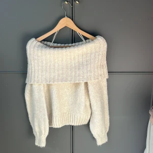 Beige stickad offshoulder tröja - Säljer en superfin beige stickad tröja med offshoulder-design. Perfekt för en mysig och stilren look. Tröjan har en bred ribbad kant upptill och långa ärmar. Passar perfekt till både jeans och kjol!💕