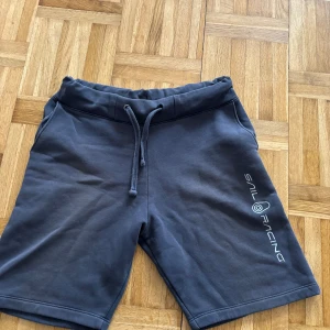 Grå shorts från Sail Racing - Snygga grå shorts från Sail Racing med snörning i midjan. Perfekta för en avslappnad stil. Logotypen är tryckt på sidan för en sportig look.