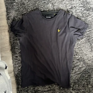 Svart t-shirt från Lyle & Scott - Säljer en stilren svart t-shirt från Lyle & Scott med deras ikoniska logga broderad på bröstet. T-shirten har en normal passform och är tillverkad i mjukt bomullsmaterial. Perfekt för en avslappnad look.