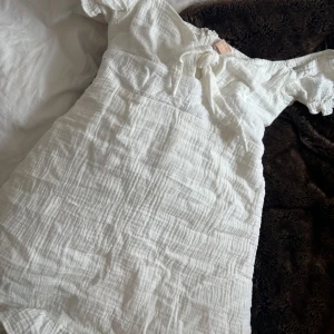 Vit klänning från Love Triangle - Säljer en söt vit klänning från Love Triangle. Klänningen har en knytning framtill och korta ärmar och lätta volanger. Perfekt nu tills studenten eller annan skola avslutning 