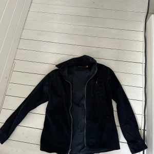 Mörkblå  manchesterjacka från Polo Ralph Lauren - Säljer en stilren svart manchesterjacka från Polo Ralph Lauren. Jackan har en dragkedja framtill och en bröstficka. Perfekt för en avslappnad och trendig look.