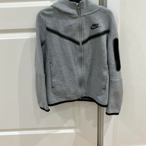 Nike teck fleece - Säljer en teck fleece från Nike med dragkedja och svarta detaljer. Tröjan har endast använd 2 gånger då den är för liten för mig. Och en liten Nike-logga på bröstet. Perfekt för en sportig look! Passar barm från 9-10. Perfekt present