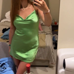 Grön kortklänning från Ginatricot - Snygg grön kortklänning med smala axelband och en lätt glansig finish. Perfekt för en utekväll eller fest. Klänningen har en enkel och stilren design som framhäver figuren.